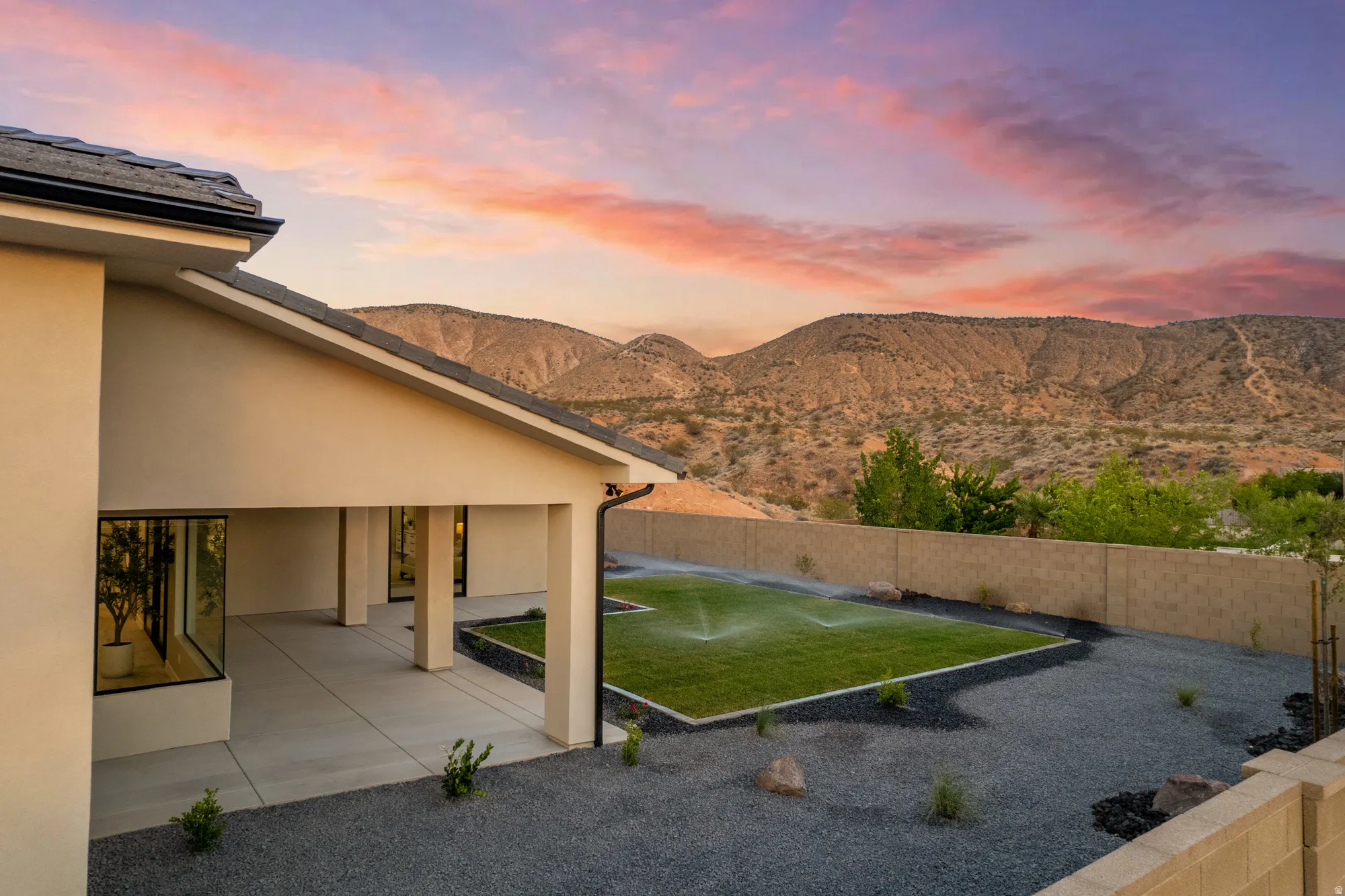 Expansive outdoor living area featuring a covered patio, a manicured lawn area with irrigation, and a surrounding landscape of gravel and desert plants