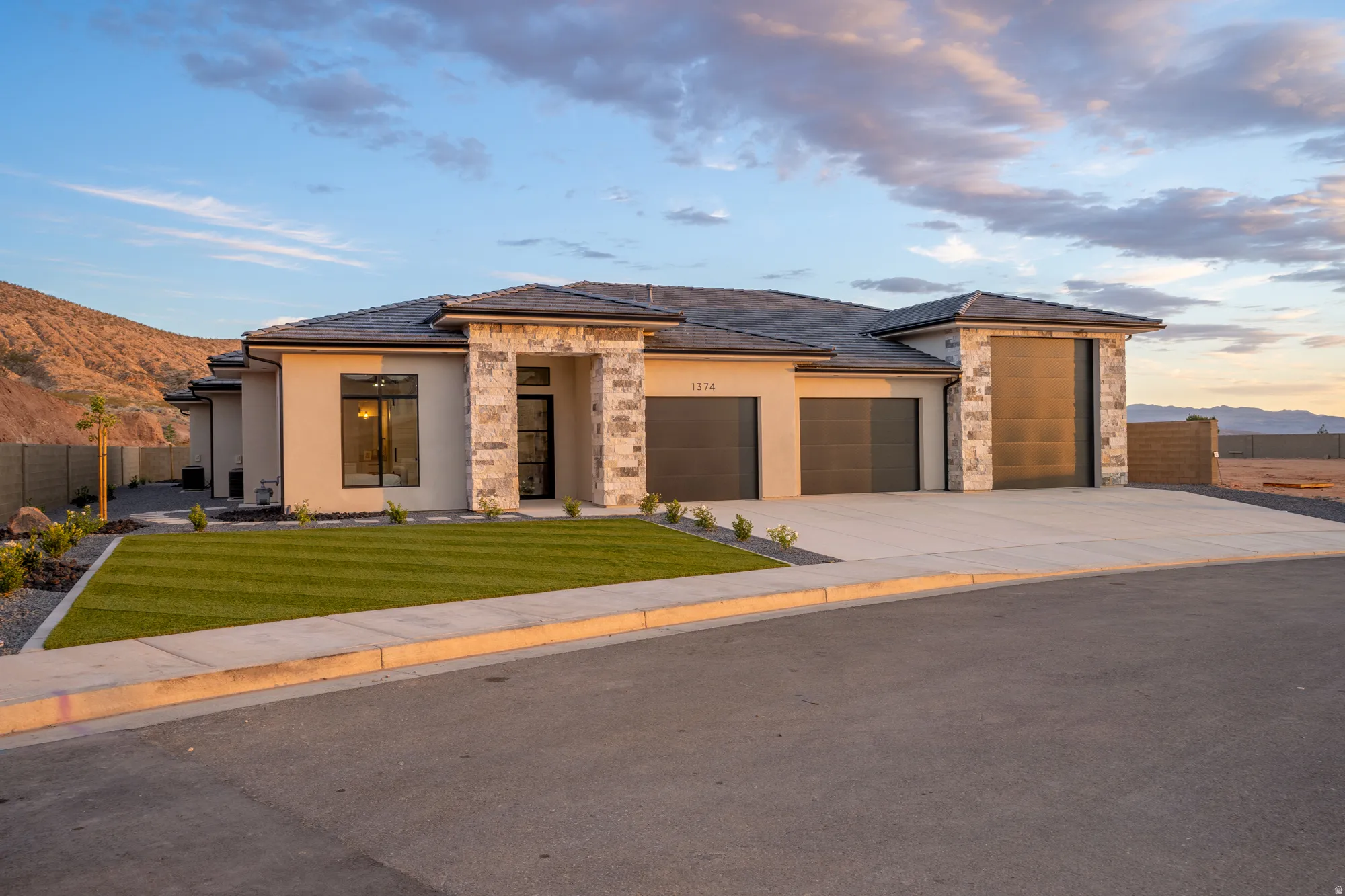 Contemporary stucco exterior featuring stone accents, a multi-car driveway, and a meticulously manicured artificial turf lawn