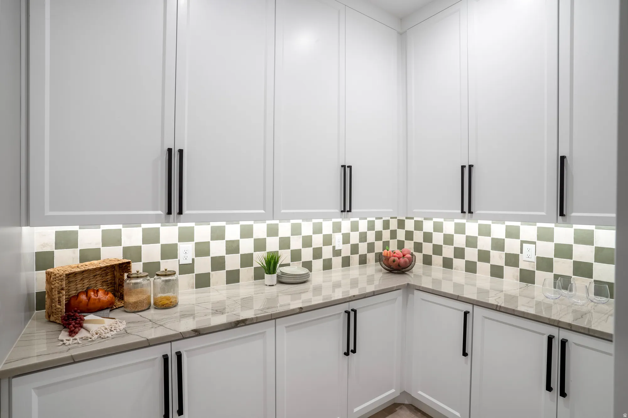 Modern kitchen with white shaker cabinetry, matte black hardware, under-cabinet lighting, a checkerboard tile backsplash, and a light-toned stone countertop