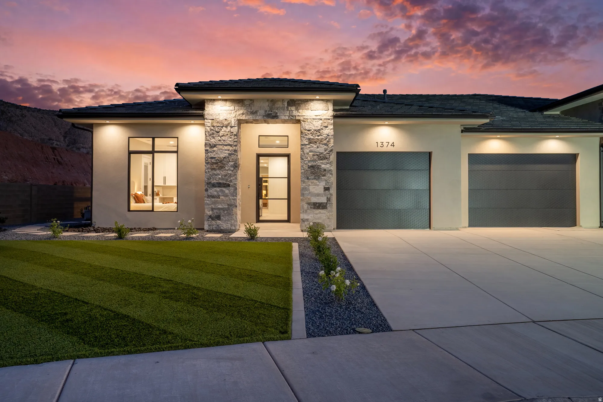Modern exterior featuring a stucco finish with stone accents, a multi-pane glass entry door, and a two-car garage