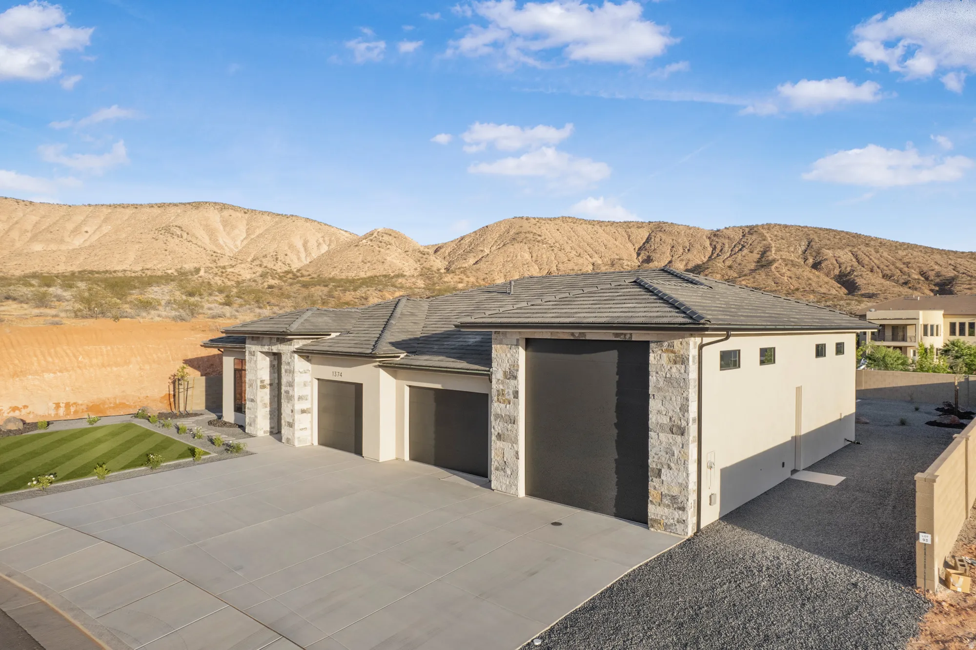 Contemporary exterior with a stone and stucco facade, featuring a multi-car garage with dark paneled doors, a gray tile roof, and a meticulously striped lawn