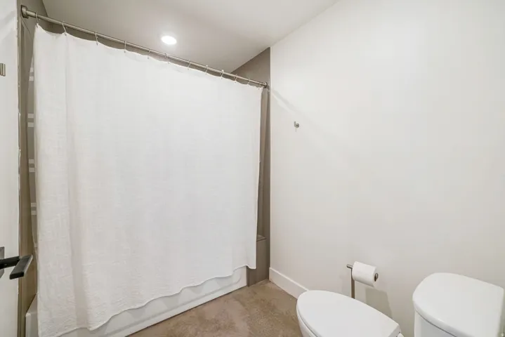 Bathroom featuring a shower-tub combination with a white curtain, recessed ceiling lighting, a contemporary toilet, and neutral wall tones