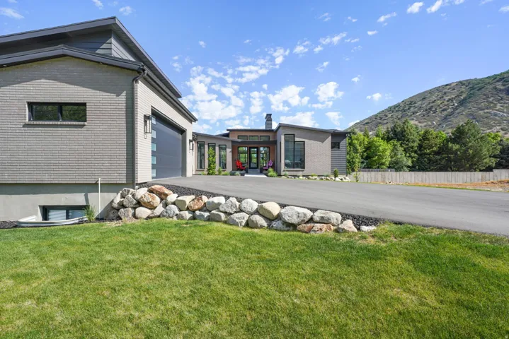 Modern architectural residence featuring multi-tone brick and siding, a multi-pane garage door, and a paved driveway with a natural rock border