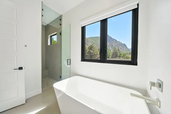 Freestanding soaking tub with a modern brushed nickel faucet and a large black-framed window showcasing mountain scenery