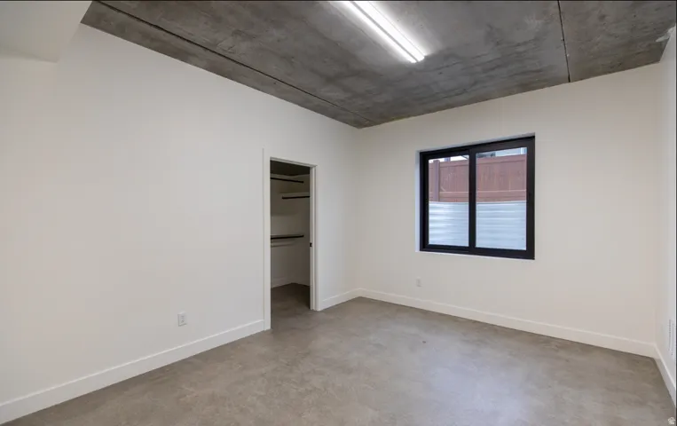 Spacious room featuring a concrete ceiling, a black-framed window with frosted lower panes, and concrete flooring