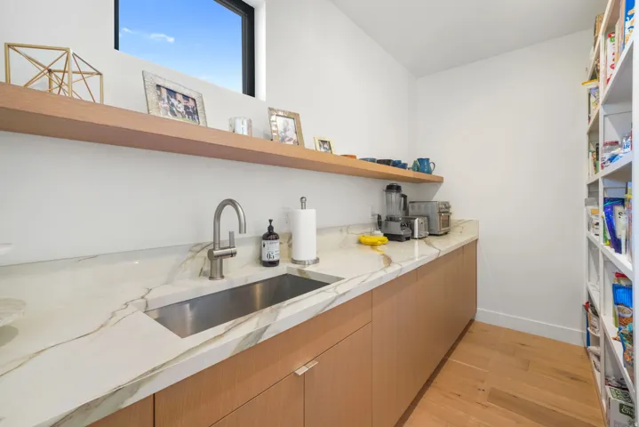 Spacious pantry featuring extensive white cabinetry, a built-in stainless steel sink, and wood-finish flooring
