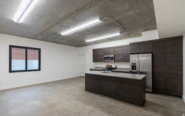 Open-concept living space featuring a contemporary kitchen with dark wood-finish cabinetry, stainless steel appliances, and a central island with a light-toned countertop
