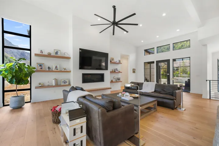 Spacious living area featuring light wood-finish flooring, a wall-mounted fireplace, and open shelving