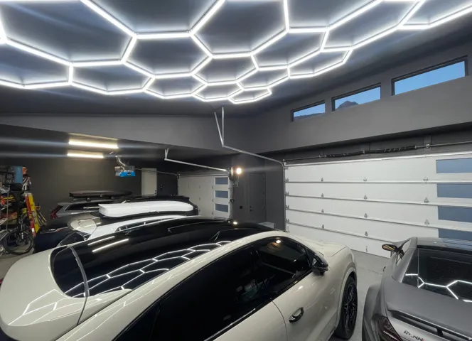 Garage featuring a honeycomb LED lighting system, multiple overhead windows, dark gray painted walls, and white sectional garage doors with frosted glass panels