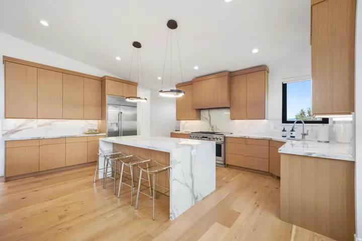 Spacious kitchen featuring an oversized island with waterfall countertop, stainless steel appliances, light wood-finish cabinetry, and recessed lighting