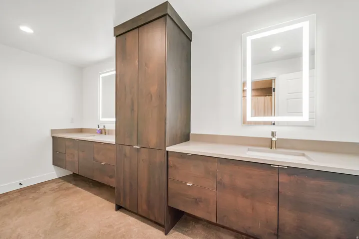 Bathroom featuring dual wood-finish vanities with integrated sinks and light-up mirrors