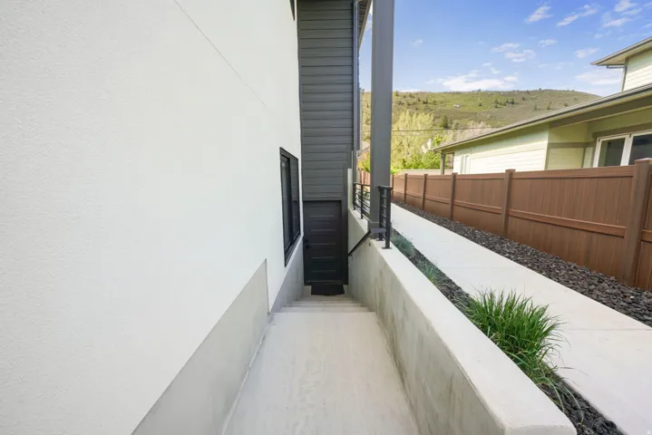 Exterior pathway featuring a concrete walkway, decorative gravel, and a dark brown privacy fence