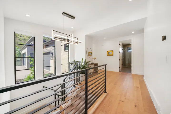 Open staircase with metal railings, wood-finish flooring, and a contemporary linear light fixture