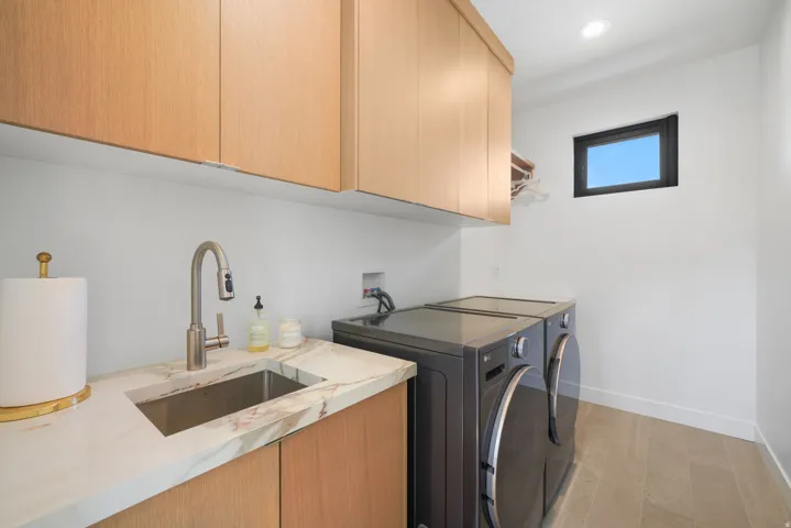 Laundry room featuring light wood-finish cabinetry, a stone countertop with an integrated sink, and wood-finish flooring