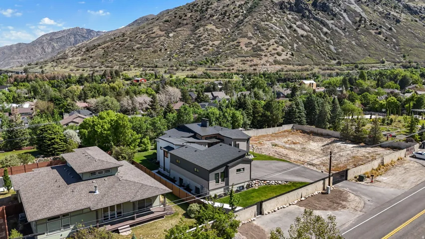Modern residence featuring a gray and white exterior with a dark shingle roof, surrounded by green landscaping and mature trees, with a mountain backdrop