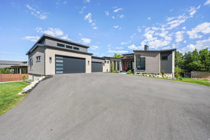 Modern architectural residence featuring a multi-tone exterior, an attached garage with a contemporary door, a large paved driveway, and established landscaping