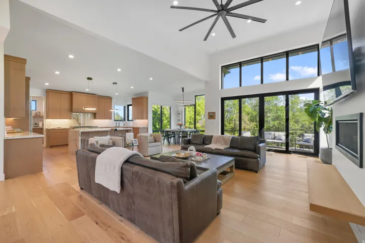 Vaulted living area featuring high ceilings, wood-finish flooring, a contemporary ceiling fan, and extensive black-framed windows overlooking exterior decking