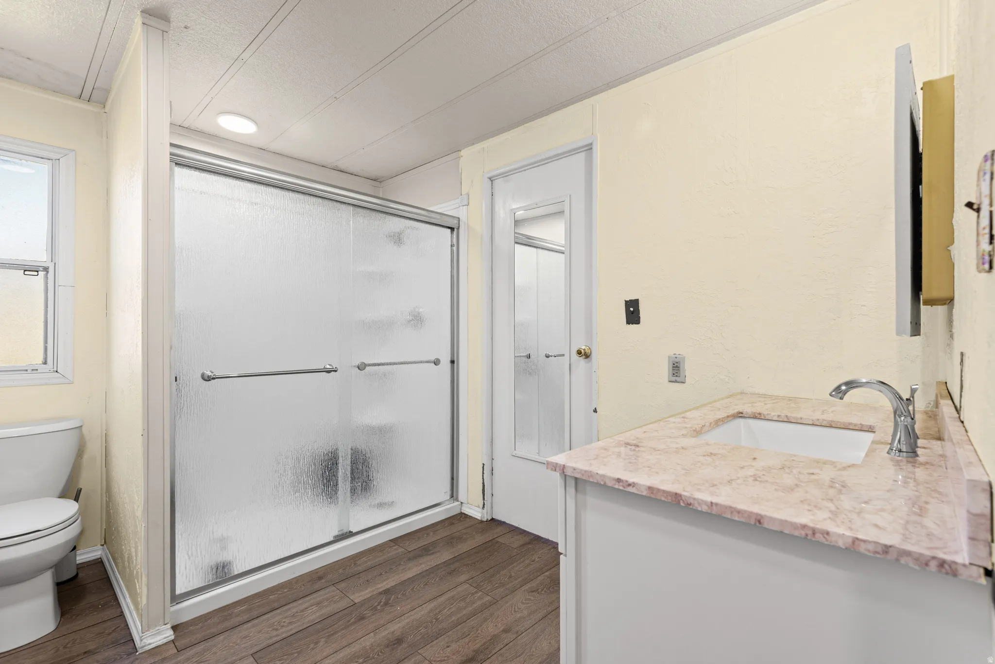 Bathroom featuring a sliding glass shower enclosure, wood-finish flooring, a vanity with a stone-finish countertop, and a recessed ceiling light
