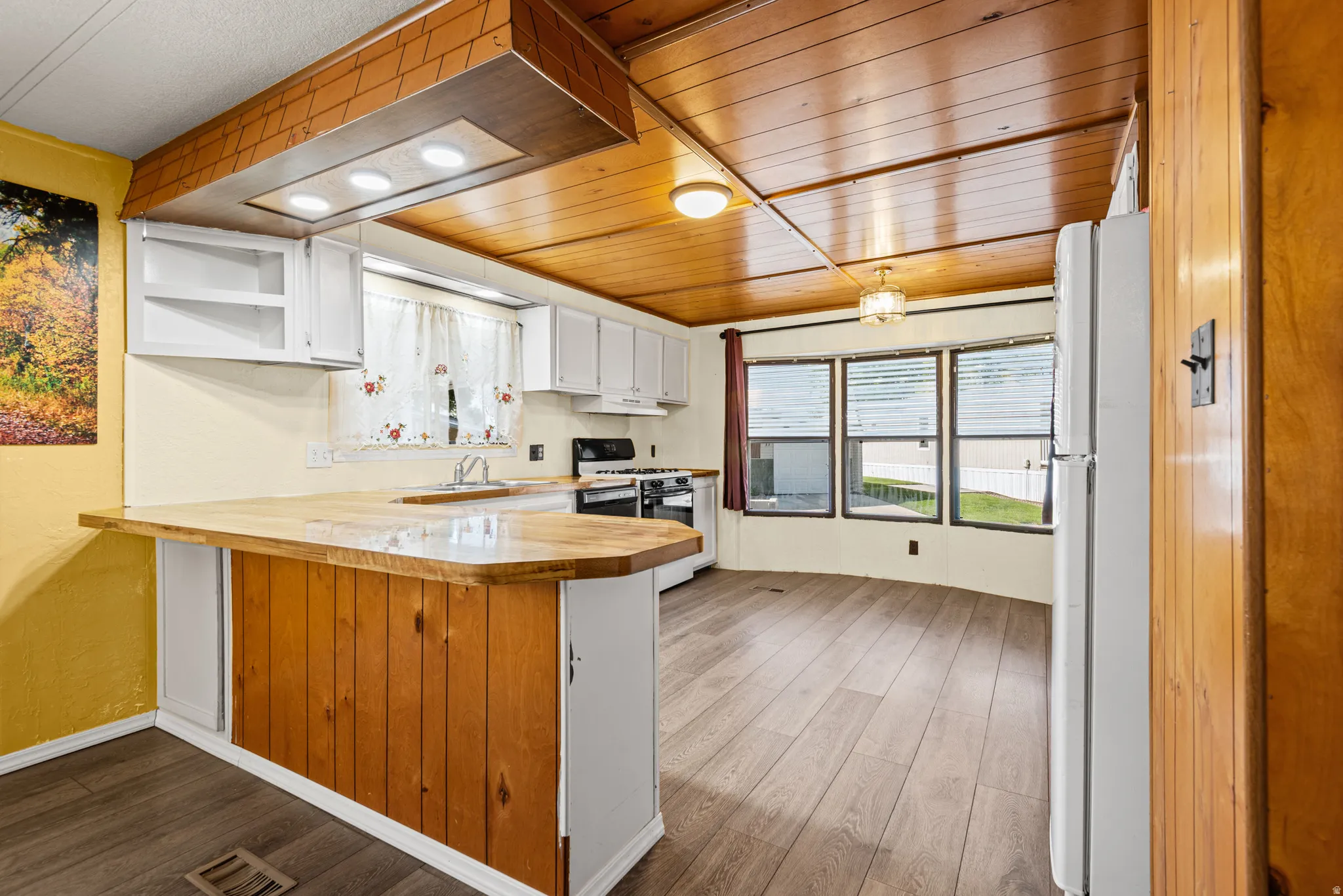 Kitchen featuring wood-finish flooring, white cabinetry, a wood-finish breakfast bar, a gas range, and a bay window