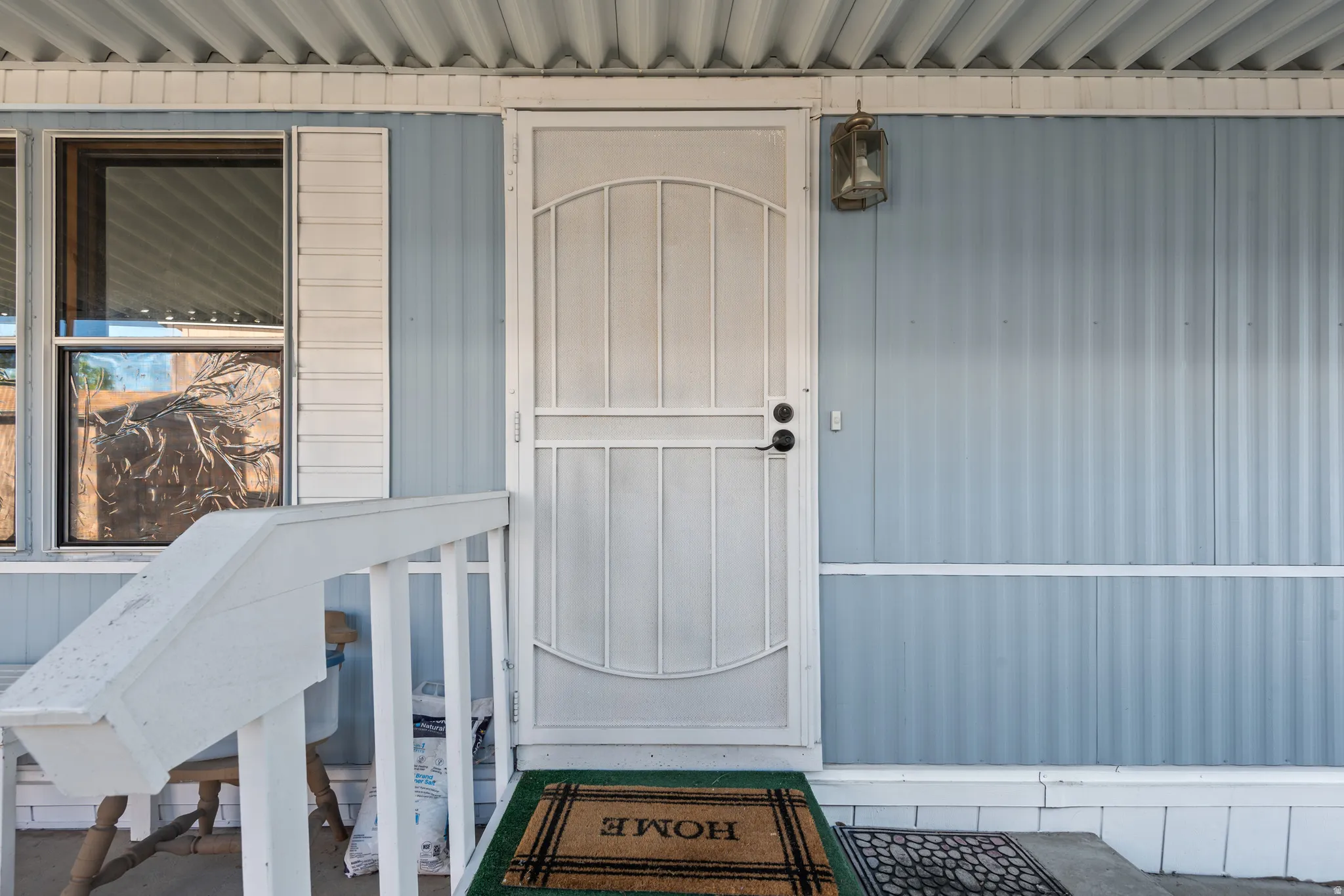 Front entry featuring a security screen door, exterior wall lighting, light blue siding, white window trim, and a covered porch
