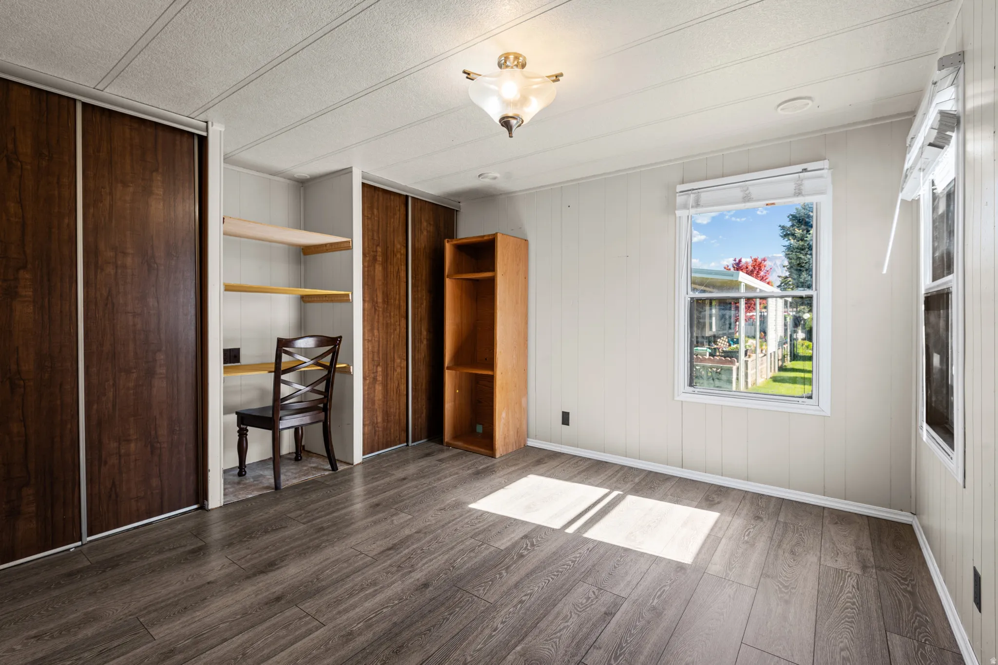 Room featuring wood-finish flooring, white paneling, and an integrated desk area with shelving
