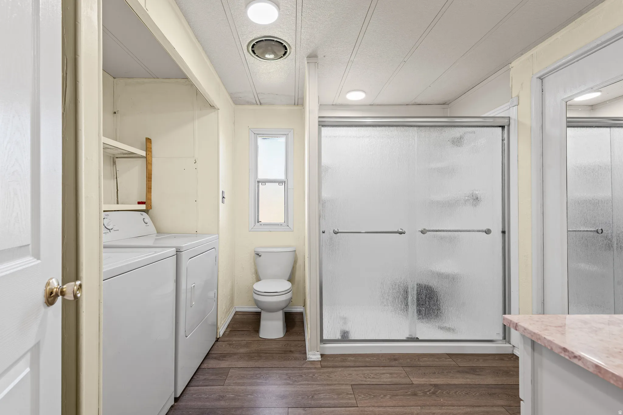 Compact bathroom featuring a shower with sliding frosted glass doors, a toilet, a window, and wood-finish flooring