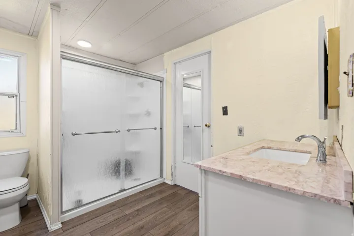Bathroom featuring a sliding glass shower enclosure, wood-finish flooring, a vanity with a stone-finish countertop, and a recessed ceiling light