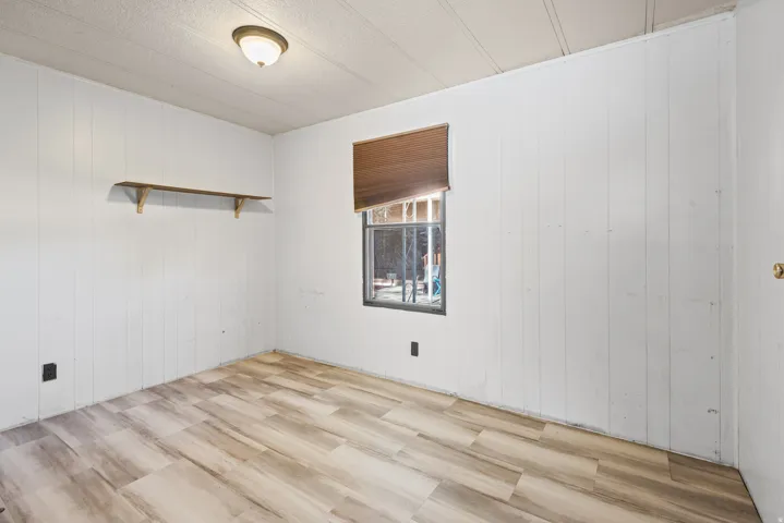 Room featuring wood-finish flooring, white vertical paneled walls, and a recessed window with a brown blind