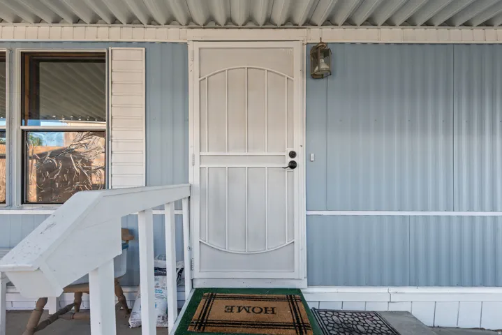 Front entry featuring a security screen door, exterior wall lighting, light blue siding, white window trim, and a covered porch