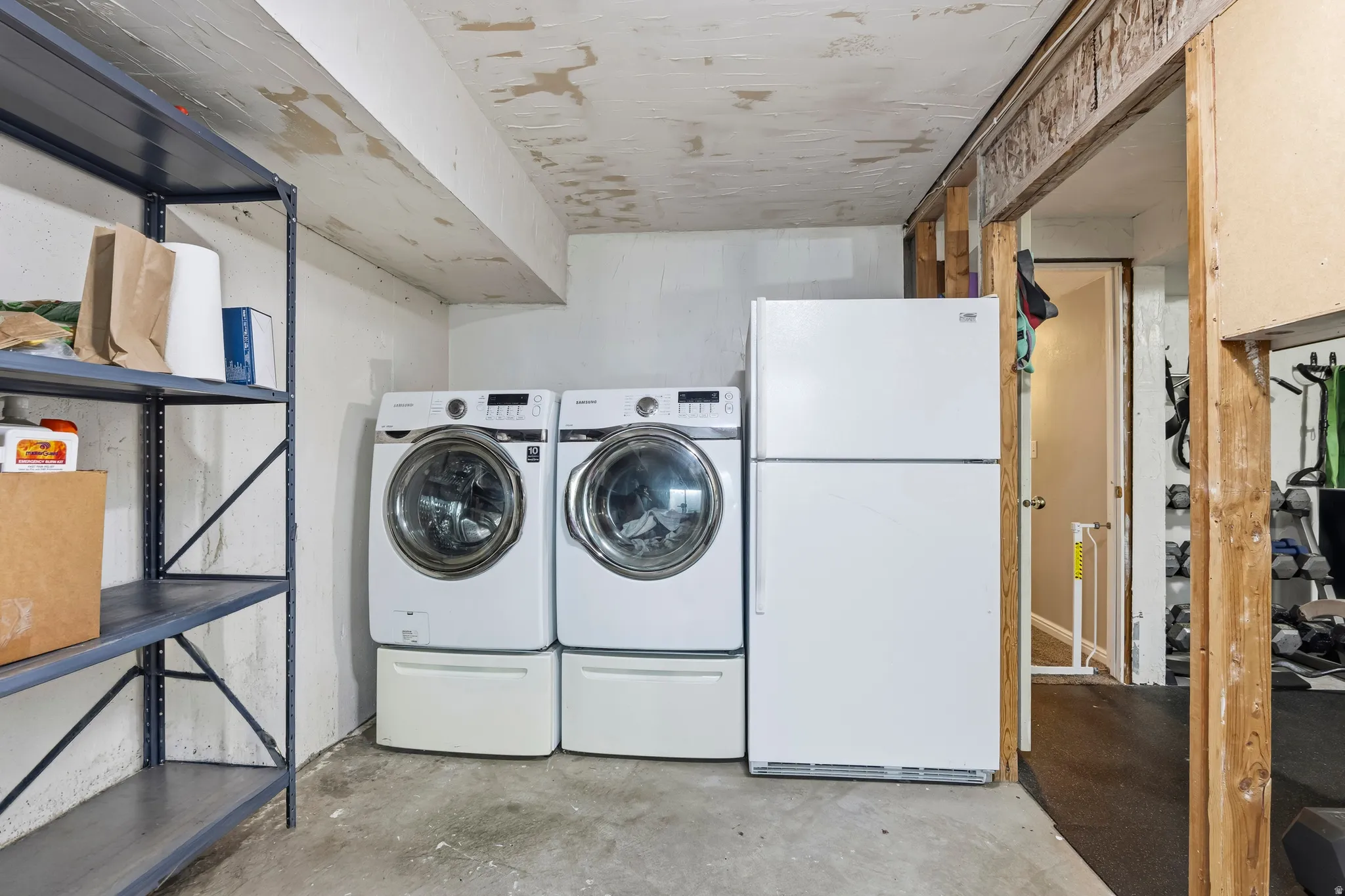 Dedicated laundry area featuring a white front-loading washer and dryer set with pedestals, complemented by a freestanding white refrigerator