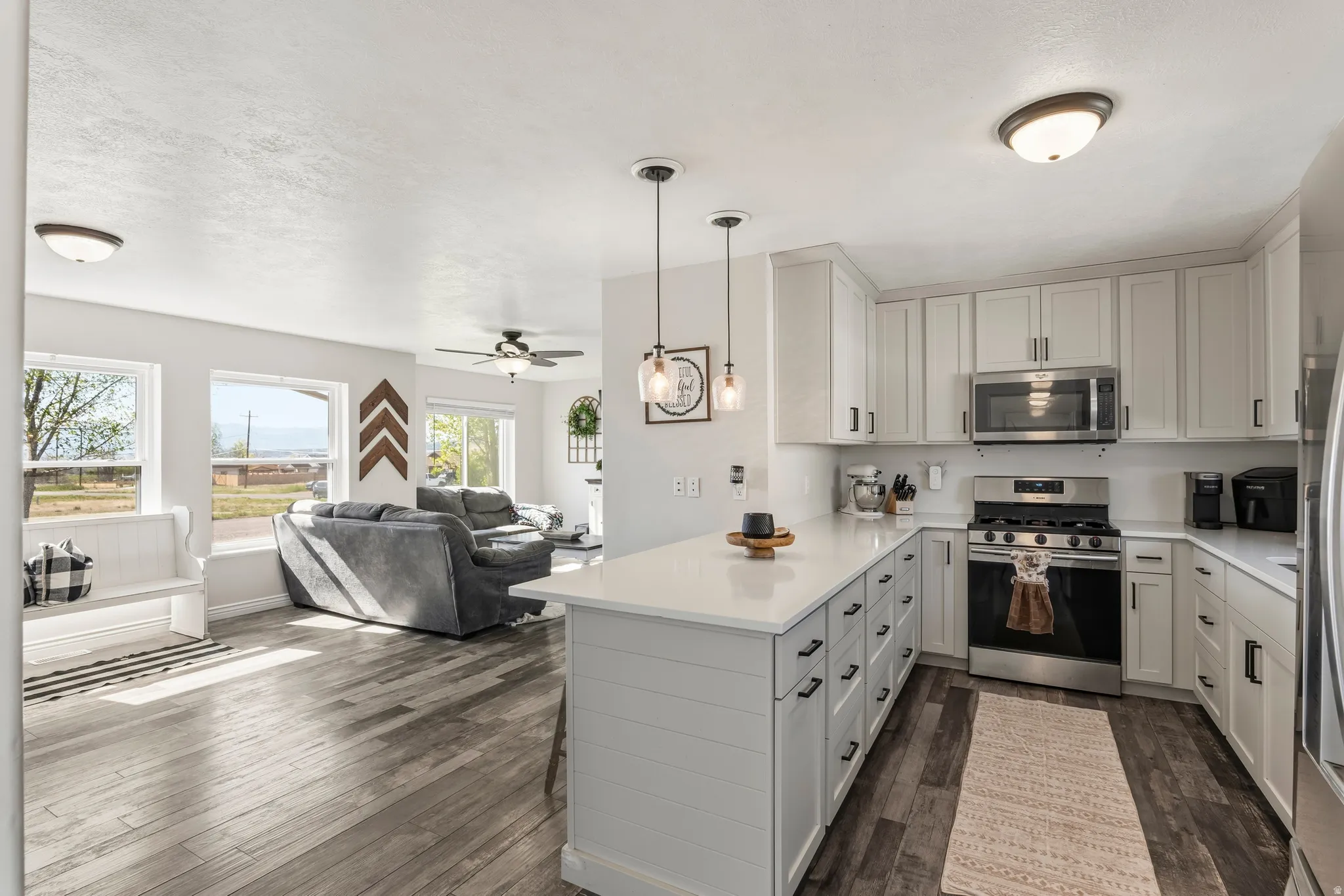 Open-concept living space featuring a kitchen with light-toned cabinetry, stainless steel appliances, a center island with pendant lighting, and wood-finish flooring extending into the living area