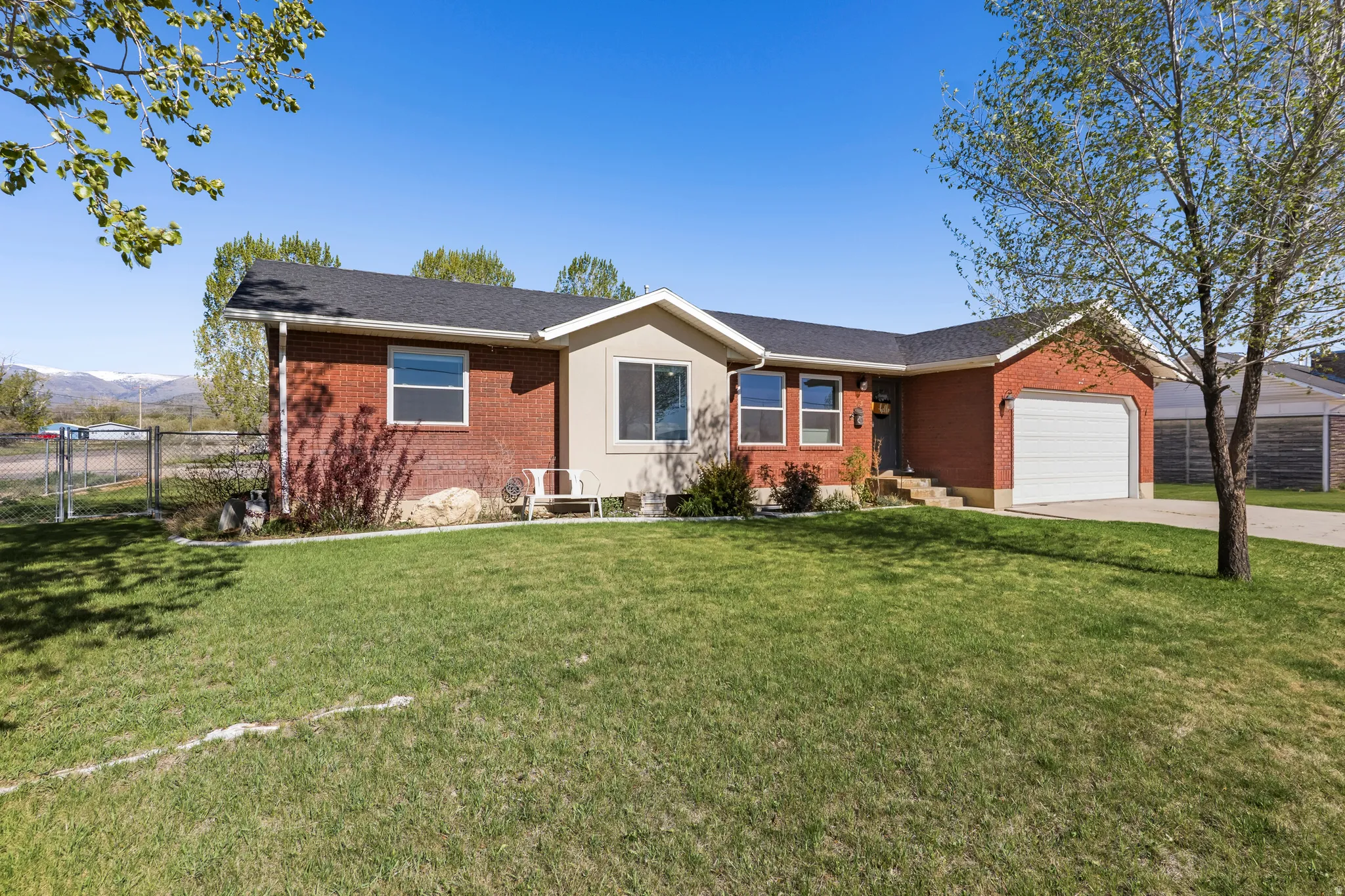 Traditional brick exterior with an attached garage, featuring a mature front lawn, paved driveway, and mountain backdrop
