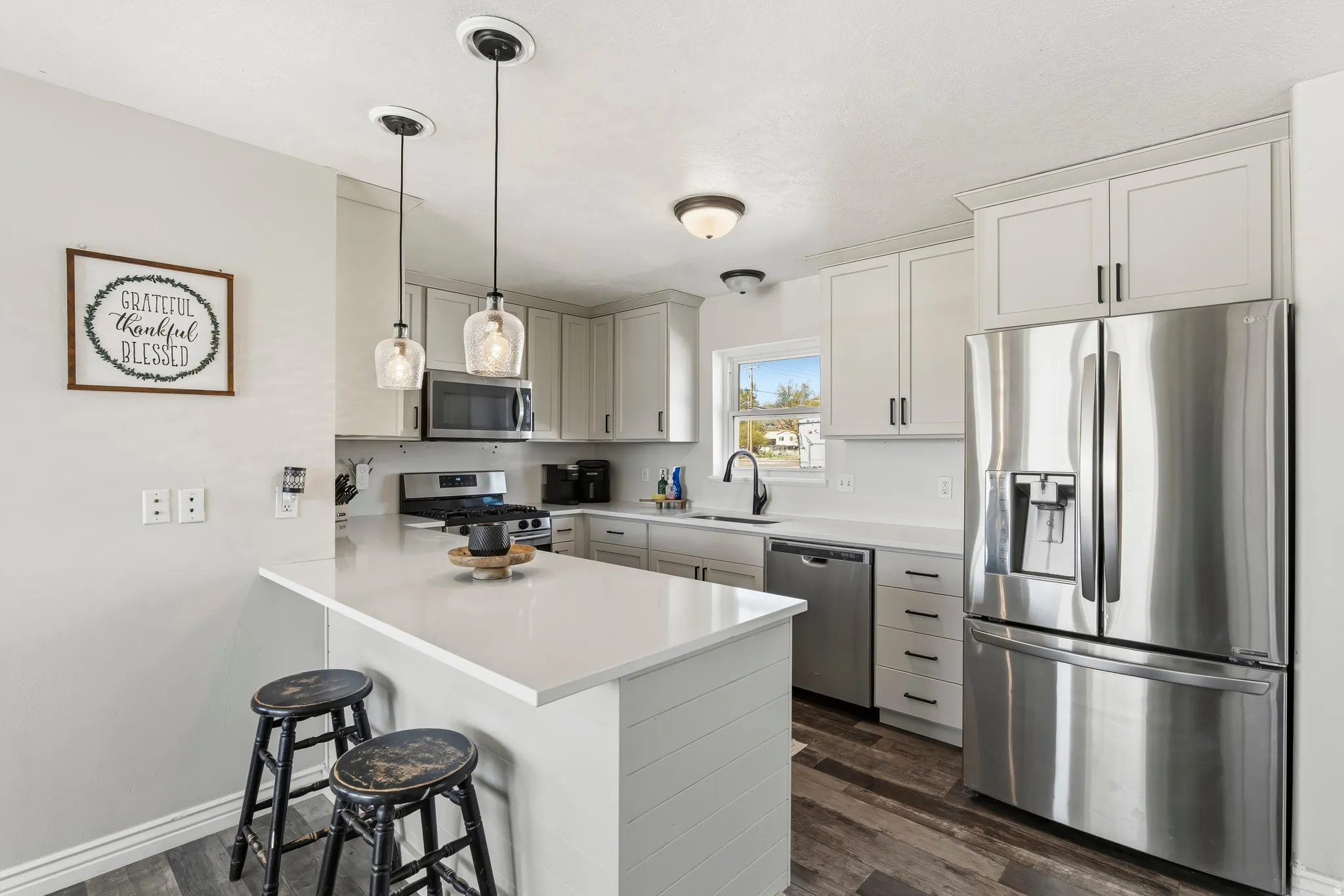 Modern kitchen featuring white shaker cabinetry, stainless steel appliances, a white countertop island with pendant lighting, and wood-finish flooring