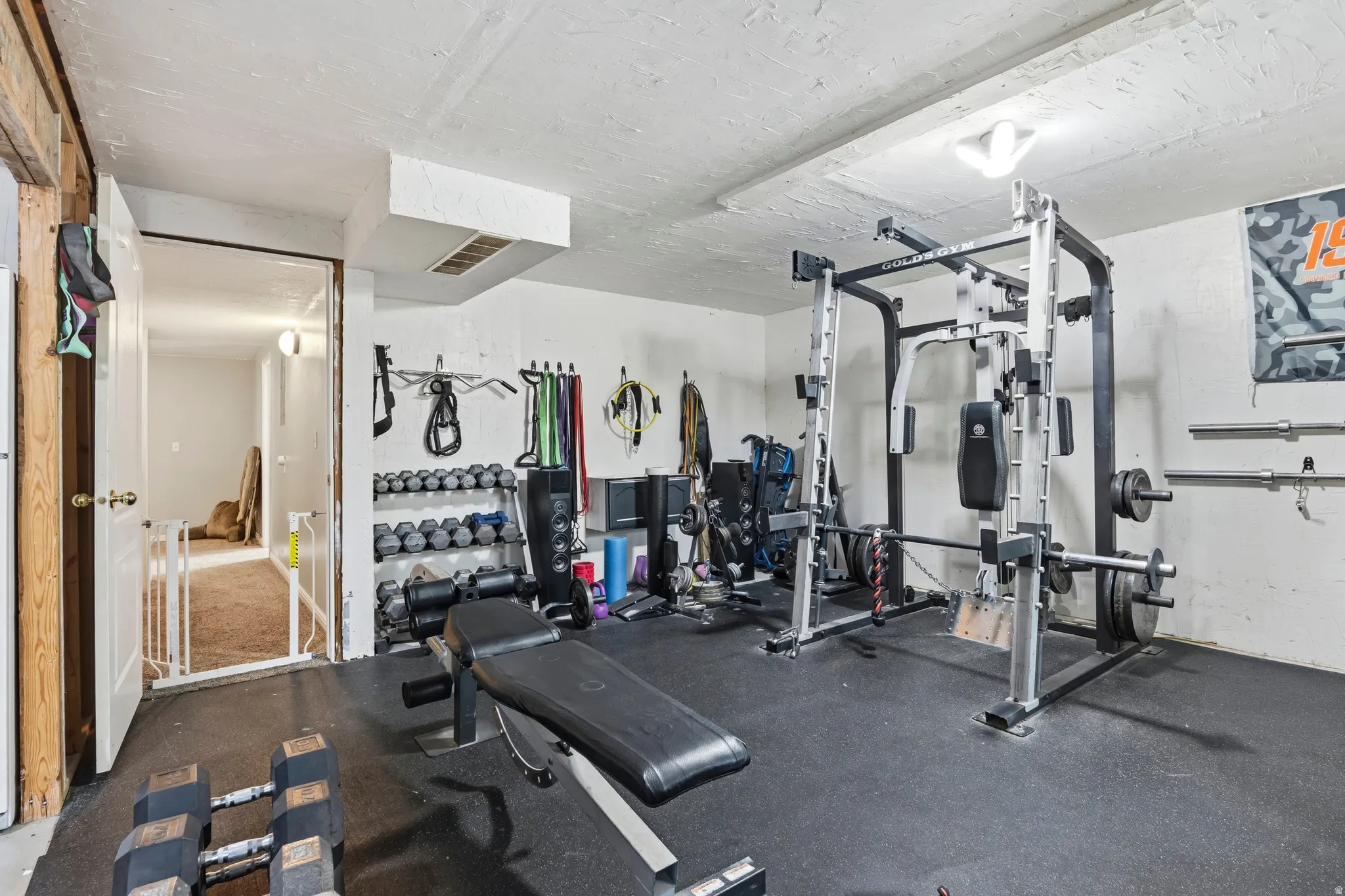 Dedicated fitness area featuring rubber flooring, a built-in dumbbell rack, and substantial wall space for equipment organization