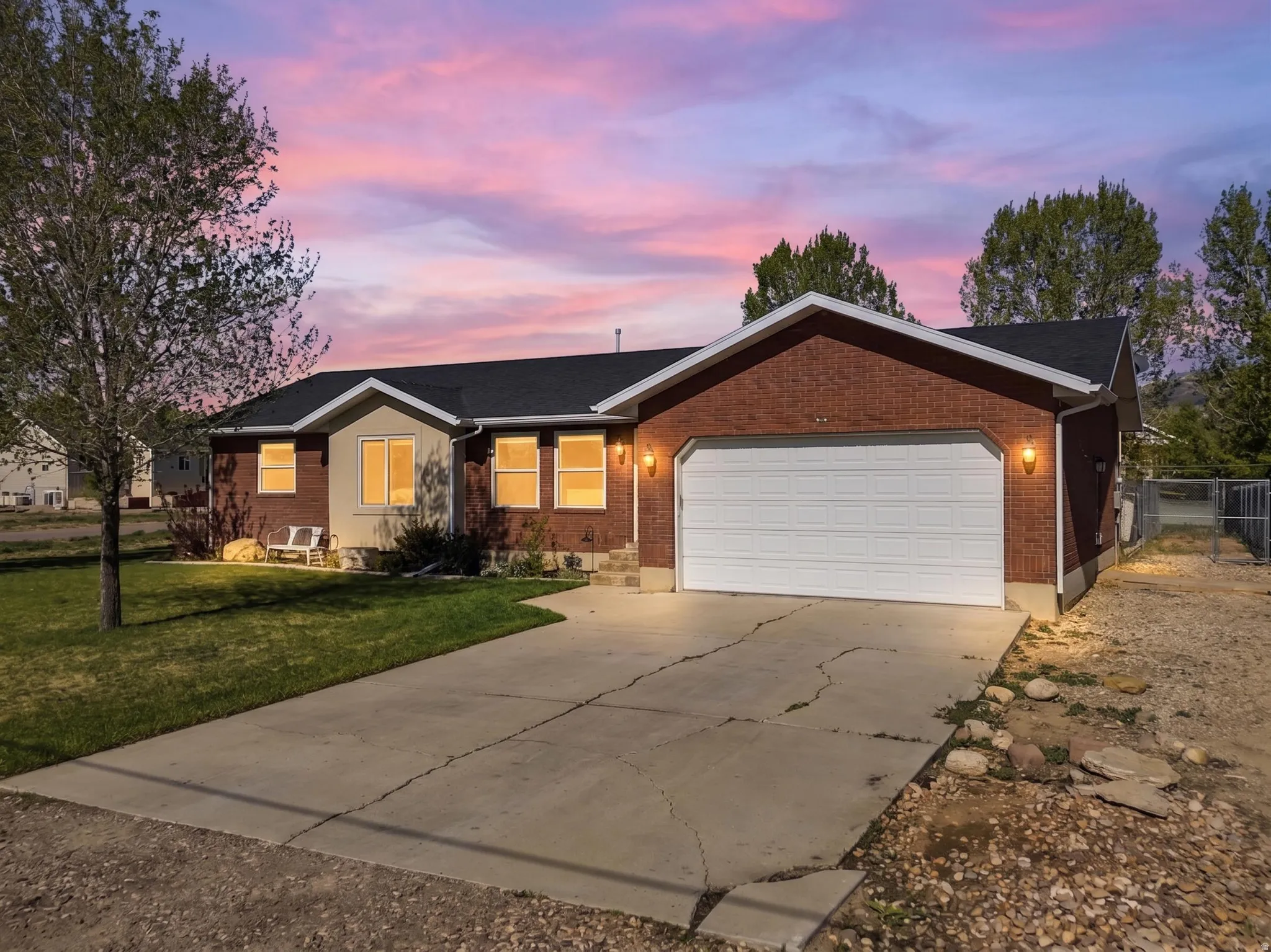 Brick facade residence featuring a two-car garage with a white door, contrasting light-colored siding, dark shingle roof, and a concrete driveway