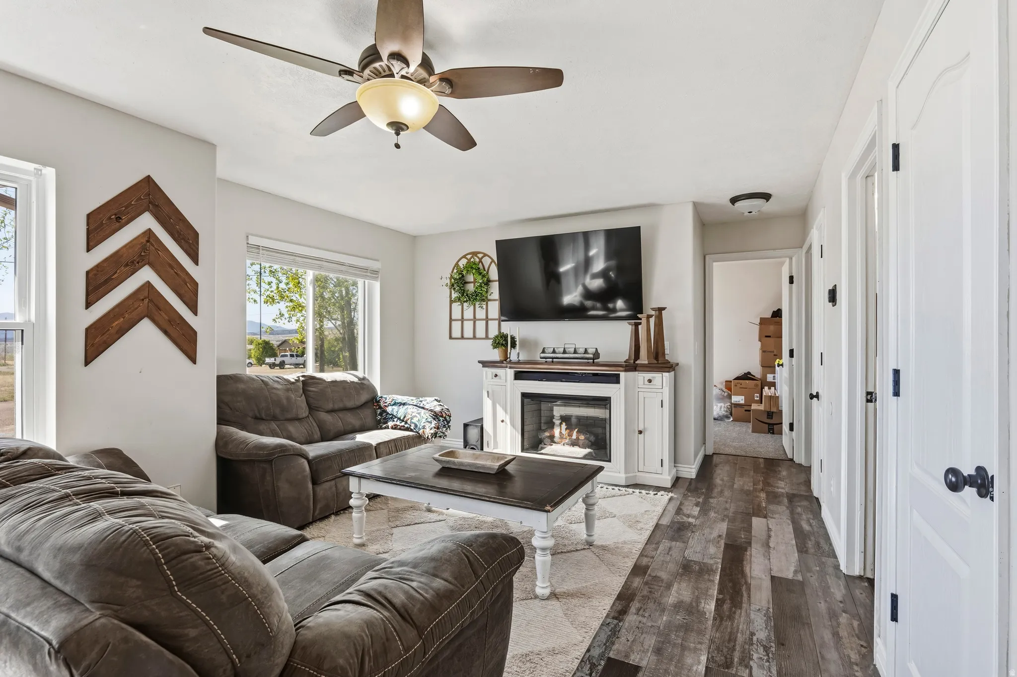 Living area featuring wood-finish flooring, a ceiling fan with integrated lighting, and multiple windows