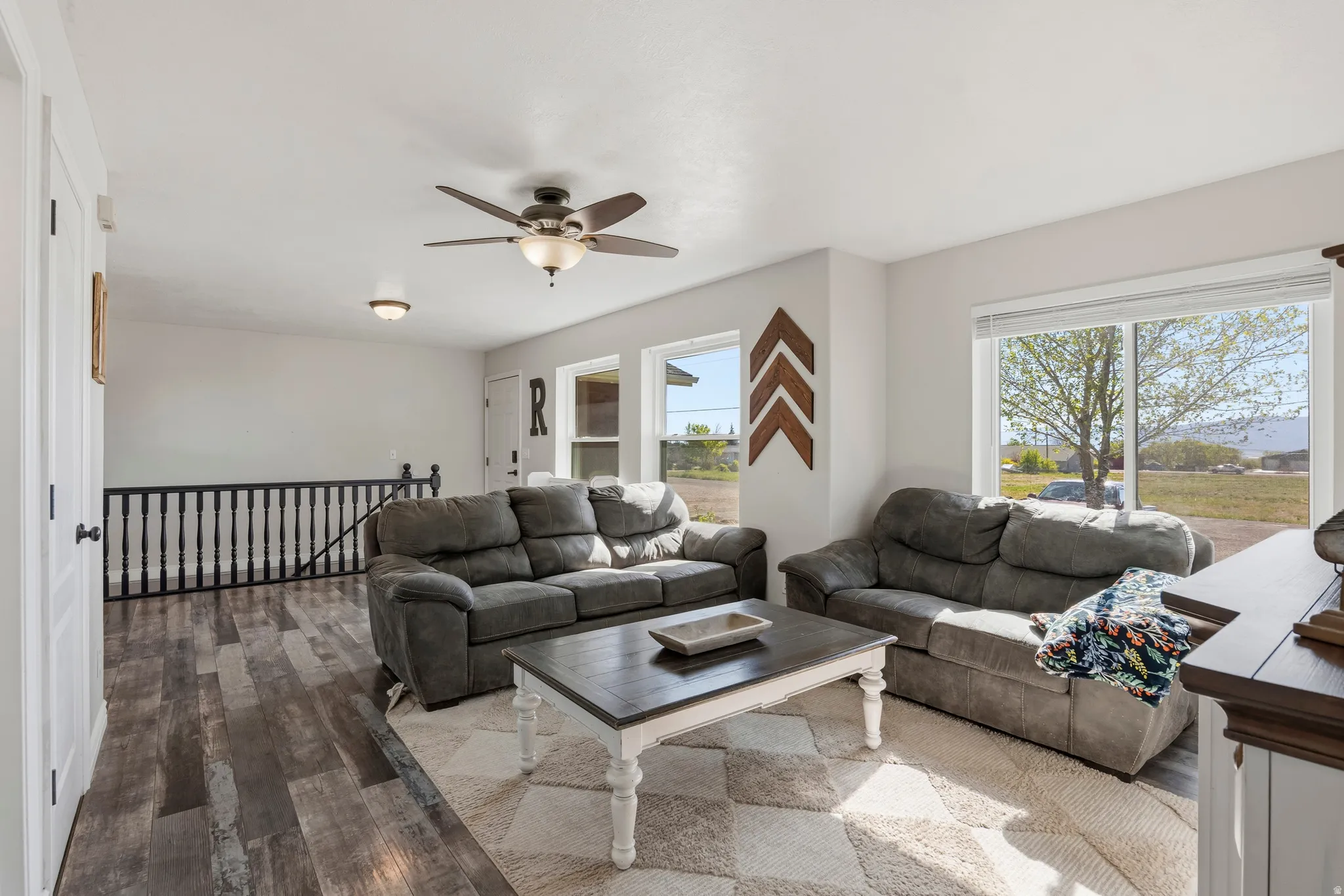 Spacious living area featuring wood-finish flooring, a ceiling fan, and large windows with outdoor scenery
