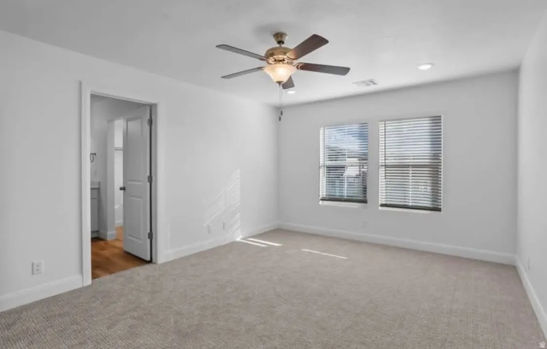 Spacious room featuring neutral carpeting, two windows with horizontal blinds, a ceiling fan with integrated lighting, and recessed ceiling lights