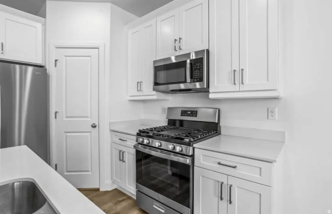Modern kitchen featuring white shaker cabinetry, stainless steel appliances, light-toned countertops, wood-finish flooring, and a stainless steel undermount sink