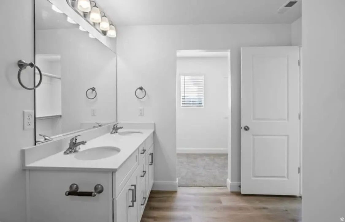 Bathroom featuring a double vanity with integrated sinks, white cabinetry, and a large wall-mounted mirror
