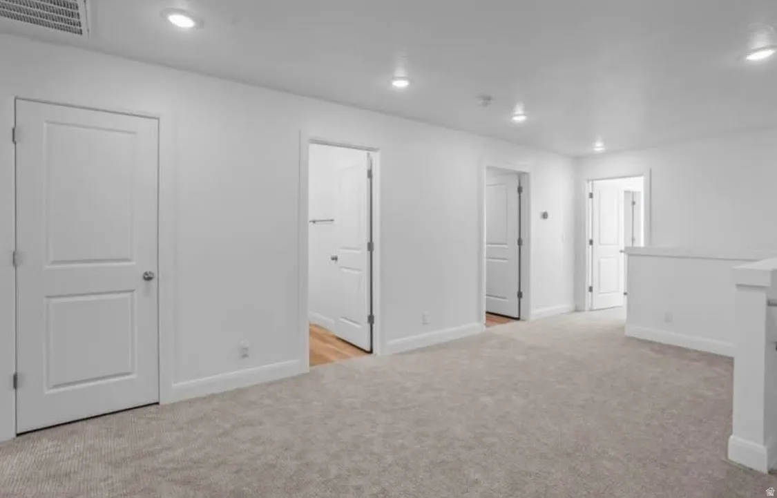 Carpeted landing area featuring white paneled doors, recessed lighting, and a white balustrade