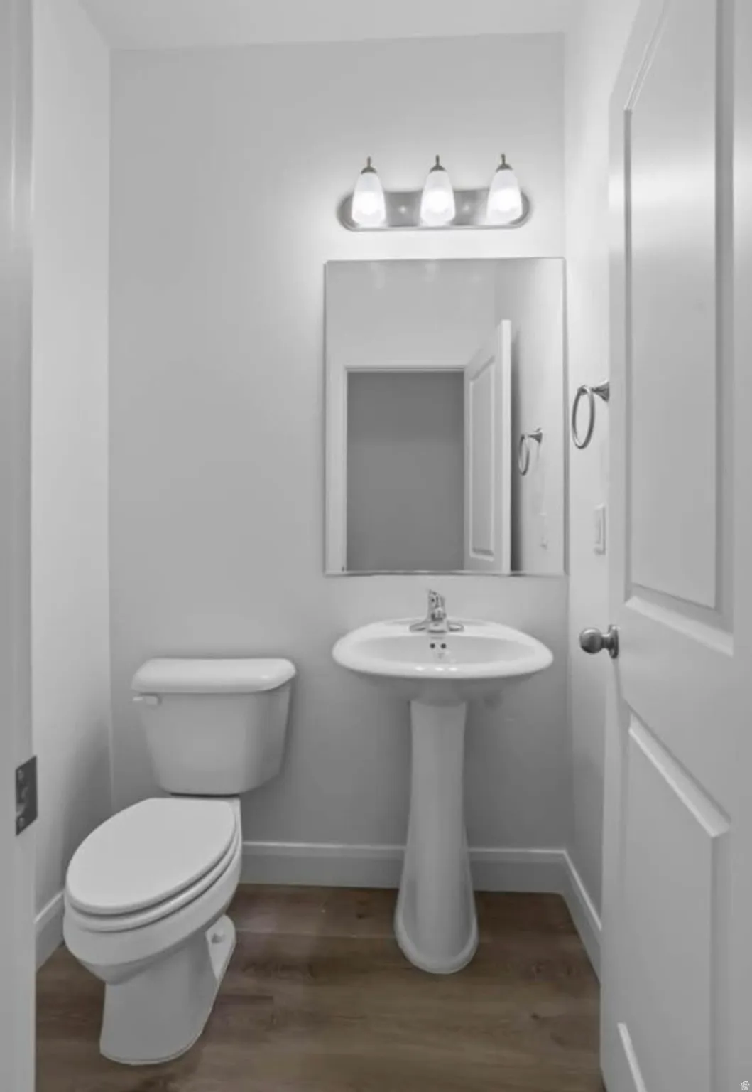 Pedestal sink with chrome faucet, a rectangular wall-mounted mirror, and a three-light vanity fixture