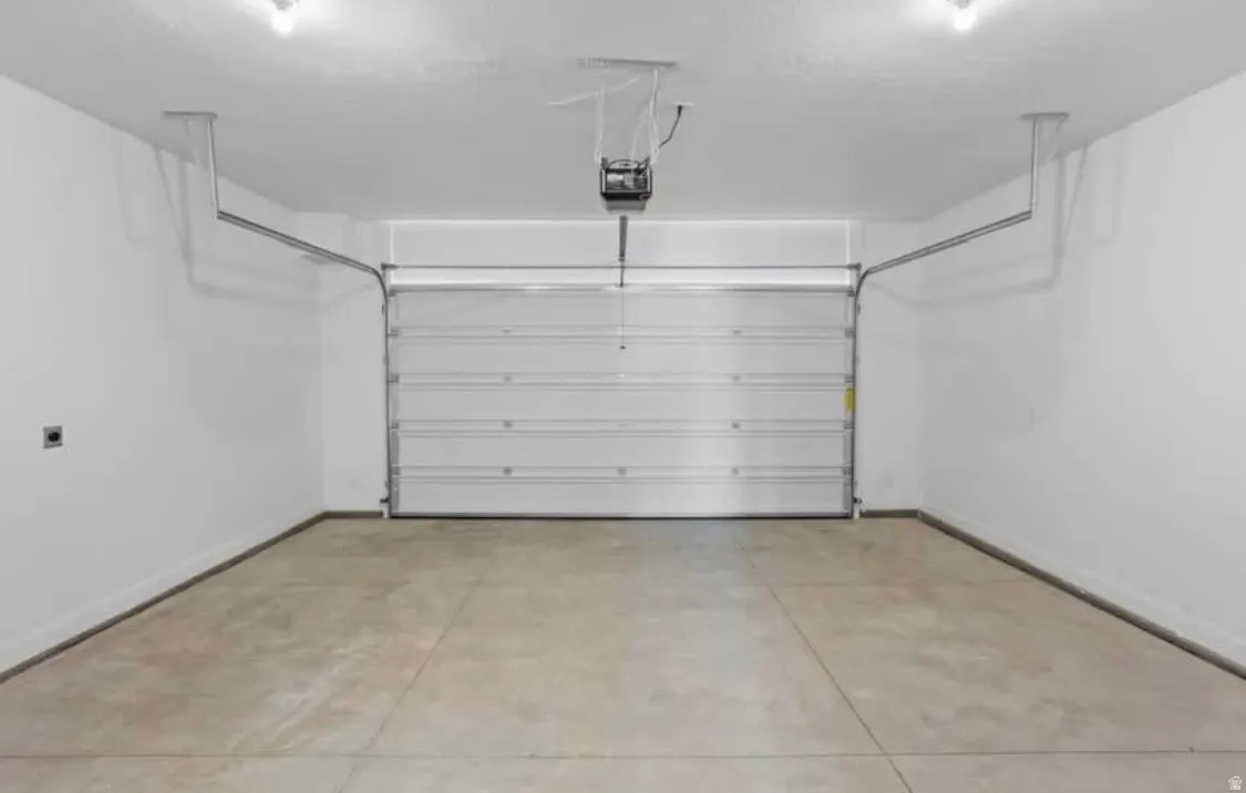 Spacious garage featuring a concrete floor, white painted walls, overhead lighting, an automatic garage door opener, and a panel garage door