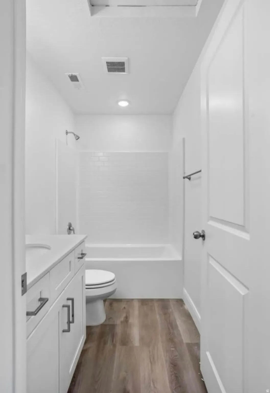 Bathroom featuring a white subway tile shower surround over a bathtub, a white vanity with shaker-style cabinetry, a white countertop, and wood-finish flooring