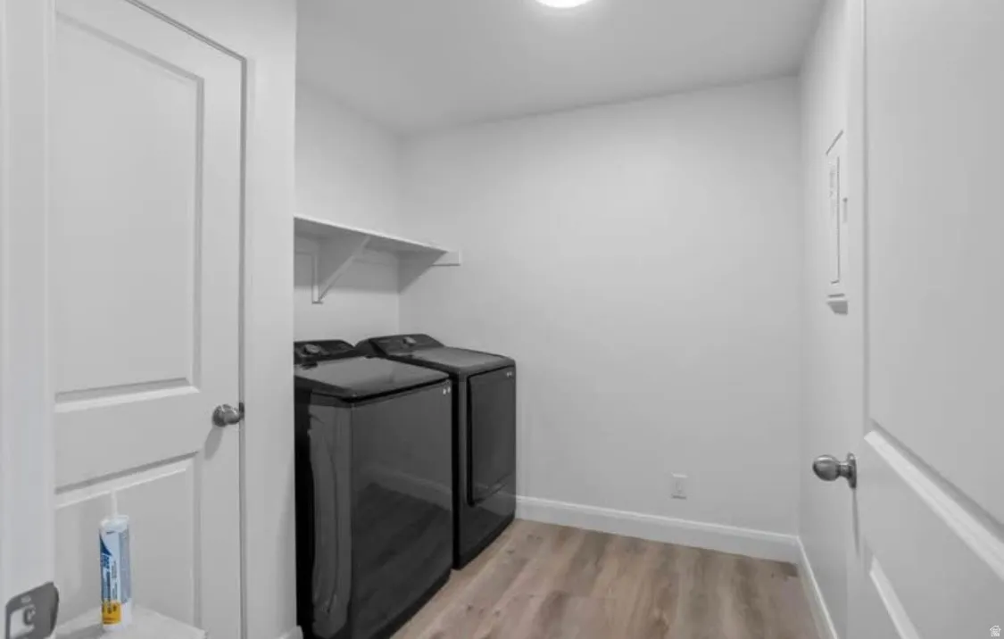 Dedicated laundry area featuring wood-finish flooring, a white wall-mounted shelf, and modern appliances