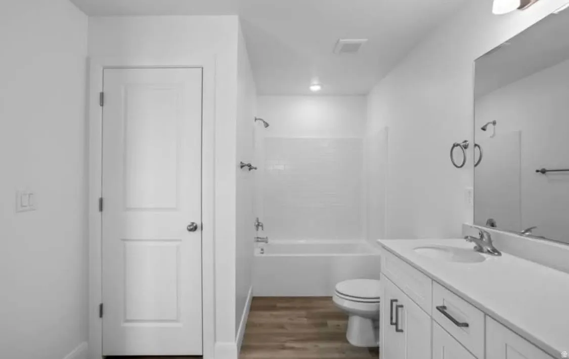 Bathroom featuring a white vanity with integrated sink, a large mirror, and a white bathtub with subway tile surround