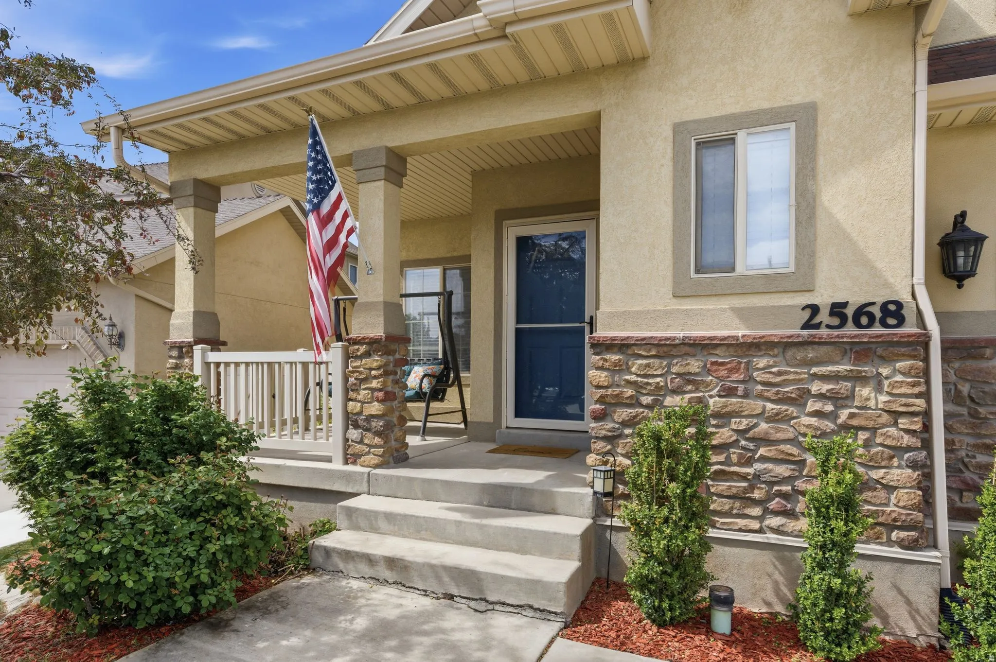 Inviting stucco exterior featuring a covered porch with stone-wrapped columns and a white railing