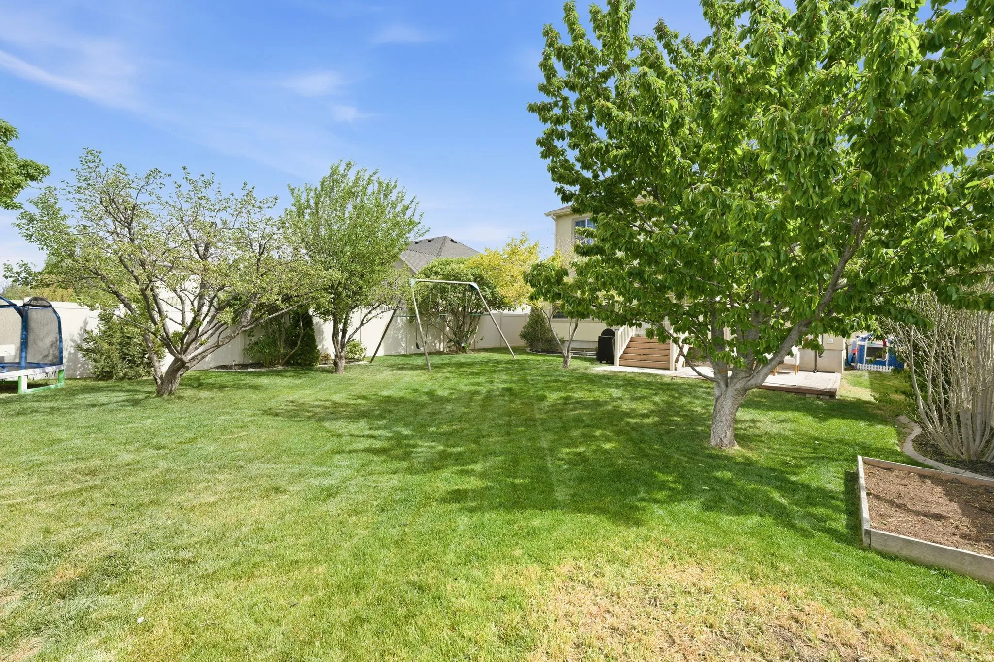 Expansive green lawn with mature trees and a raised garden bed
