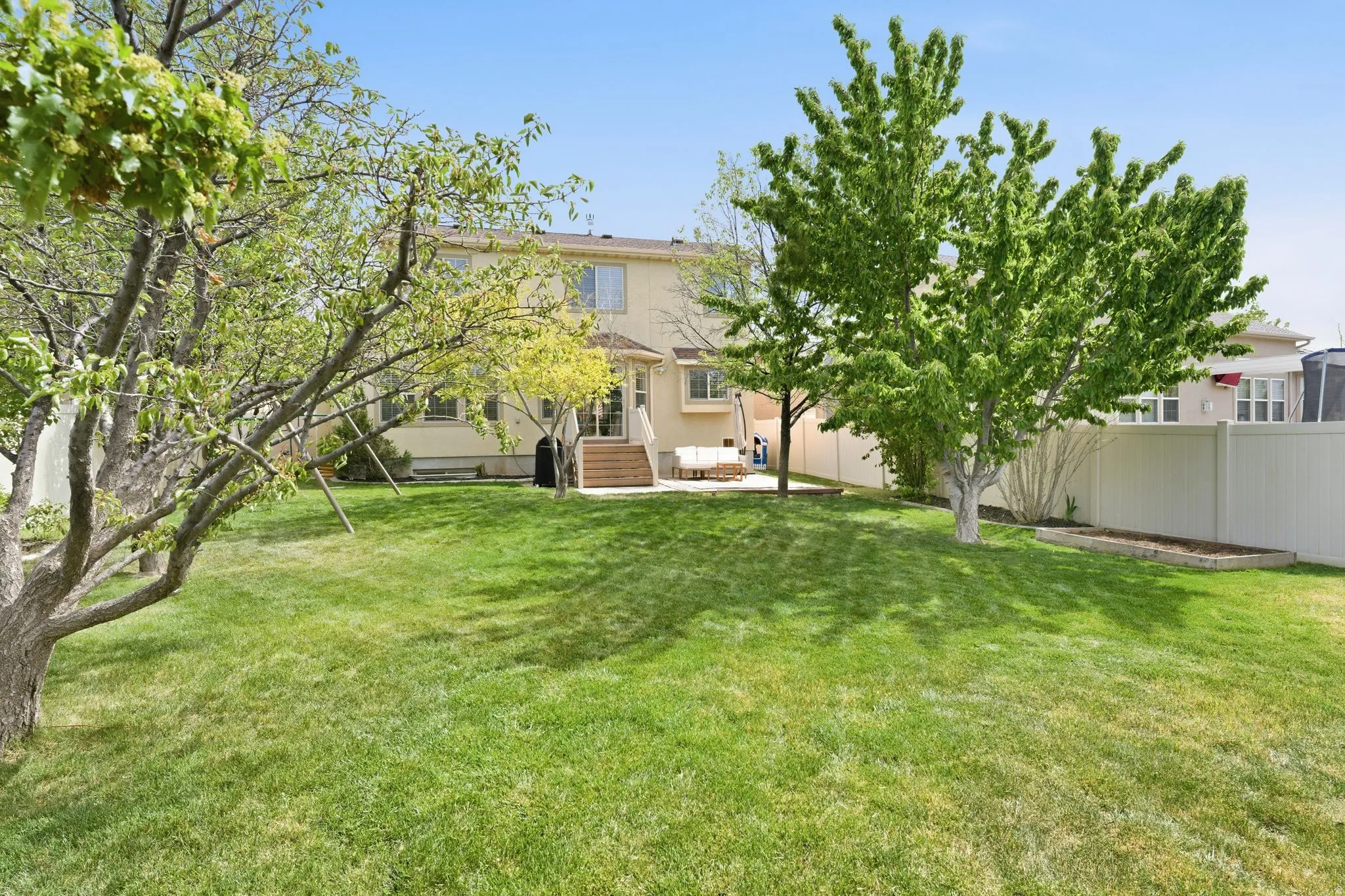 Expansive backyard featuring a lush lawn, mature trees, and a light-colored privacy fence