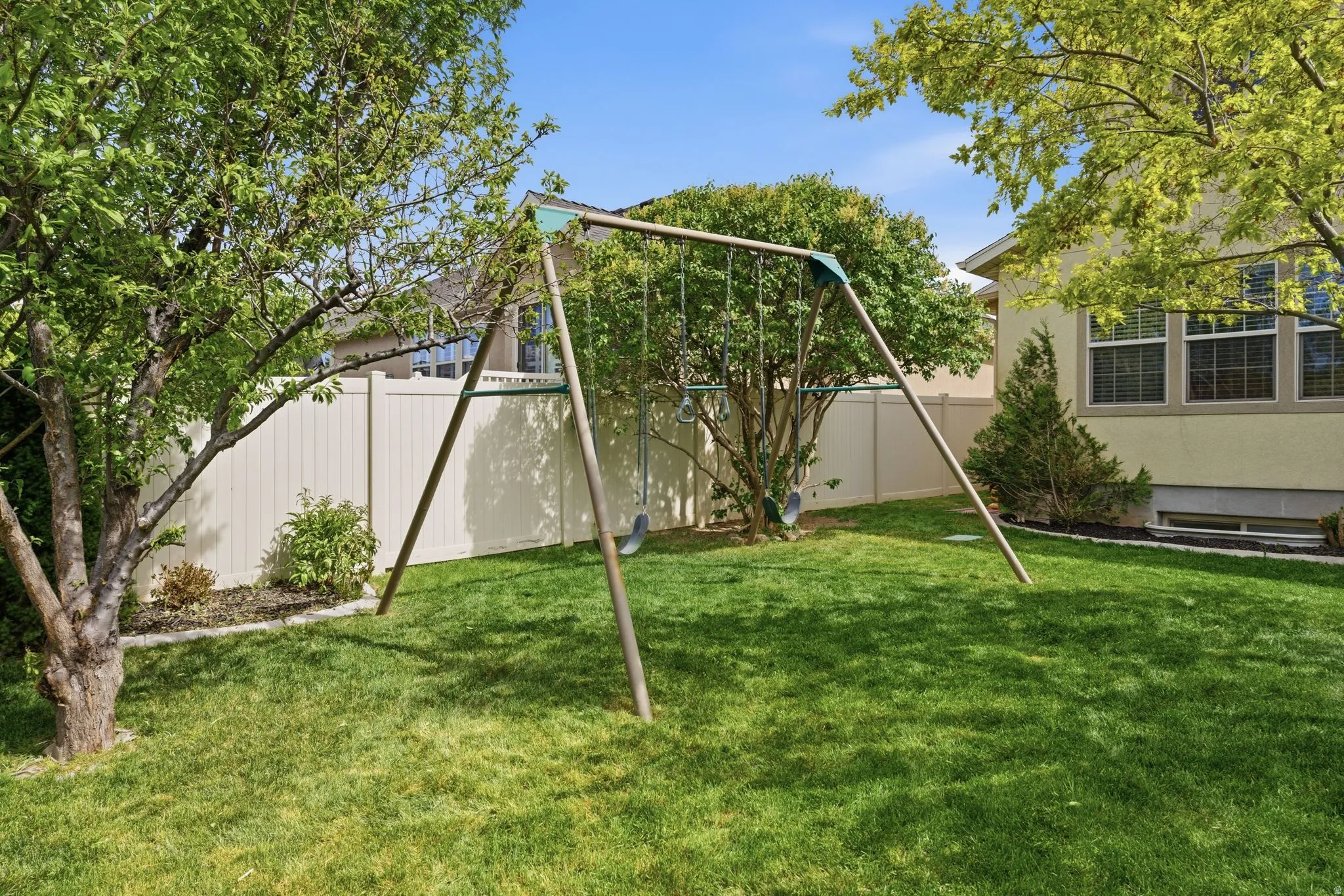 Expansive green lawn with mature trees and perimeter vinyl fencing